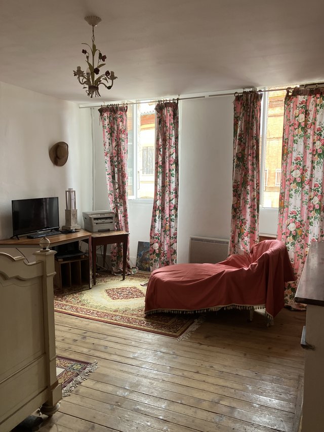 Chambre est à l’étage côté rue, avec méridienne, parquet ancien et fenêtres à rideaux fleuris donnant sur la rue