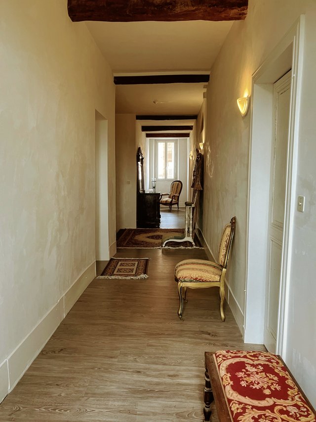 Couloir principal de l’étage avec poutres anciennes apparentes, tapis et mobilier de style, côté jardin